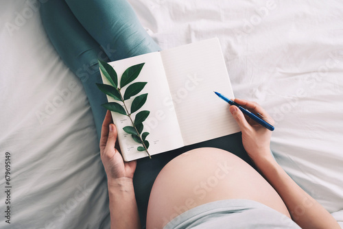 Pregnant woman with beautiful belly makes notes or check list in paper diary. Concepts of preparation for baby birth, tips for a healthy pregnancy. photo