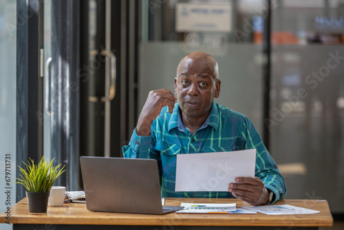 Senior black man in casual clothes holding and focus on document in hands, Verifying report, Consider the project plan as well.