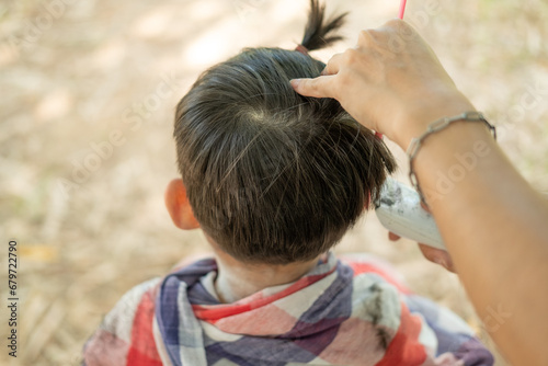Barber cutting hair of an Asian boy In an open space filled with trees.