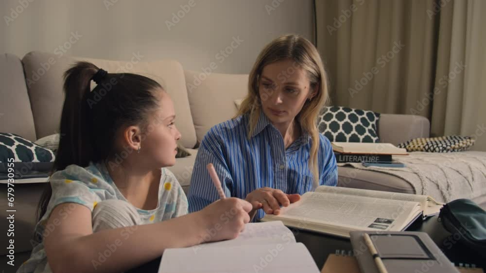 Mother her daughter with her school homework while both of them sitting next to couch in their living room Mother her daughter with her school homework while both of them sitting next to couch in their living room