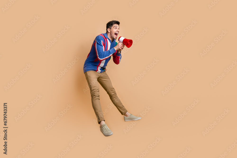 Full length photo of overjoyed energetic funky businessman jumping hold loudspeaker toa empty space isolated on beige color background Full length photo of overjoyed energetic funky businessman jumping hold loudspeaker toa empty space isolated on beige color background