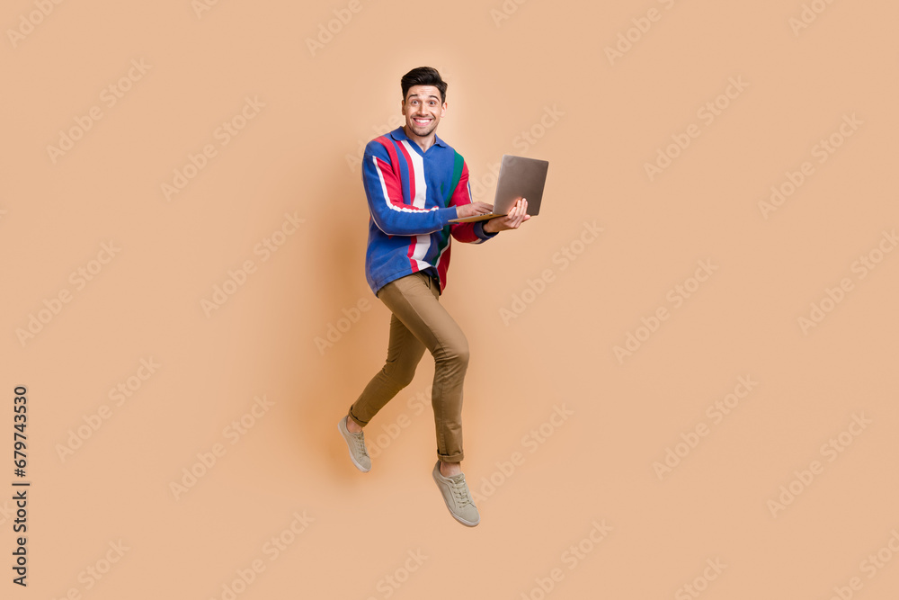 Full length photo of programmer running in air with his modern laptop to buy things with huge discounts isolated on beige color background
