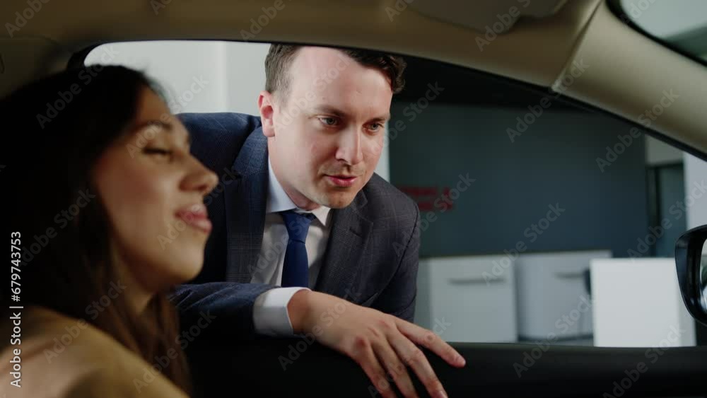 A close-up of the manager of the car center tells about the novelties of the automotive market. A woman is sitting in the driver's seat A close-up of the manager of the car center tells about the novelties of the automotive market. A woman is sitting in the driver's seat