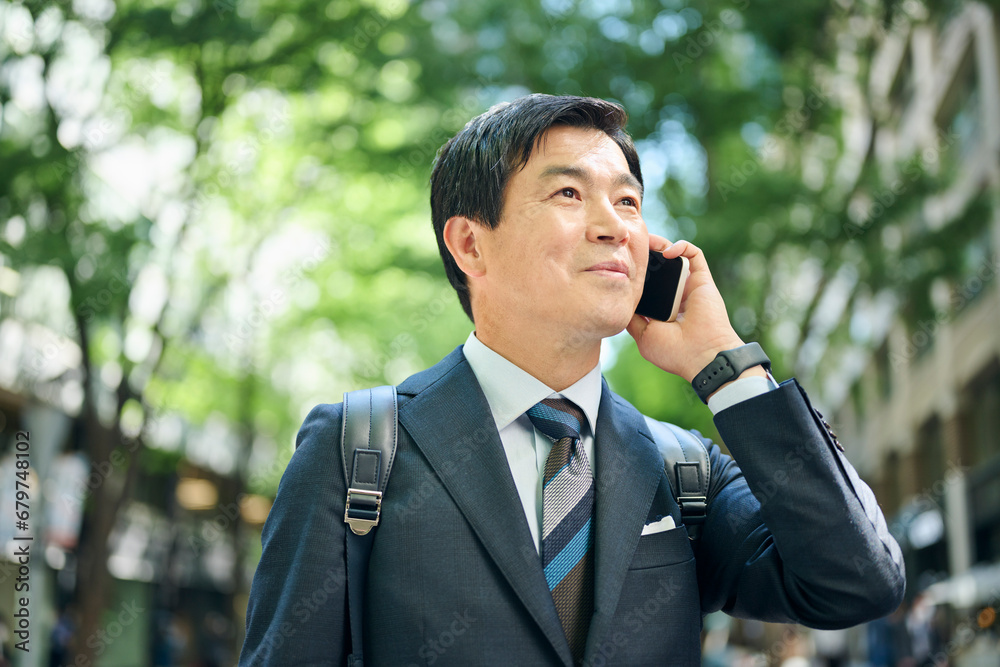 電話をしながら街中を歩く50代会社員 電話をしながら街中を歩く50代会社員