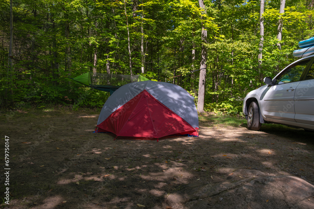 Set up campsite in the forest - tent with hanging hammock and parked SUV truck with inflated paddle boards on the roof in the background. Summer vacation, adventure, road trip concept.