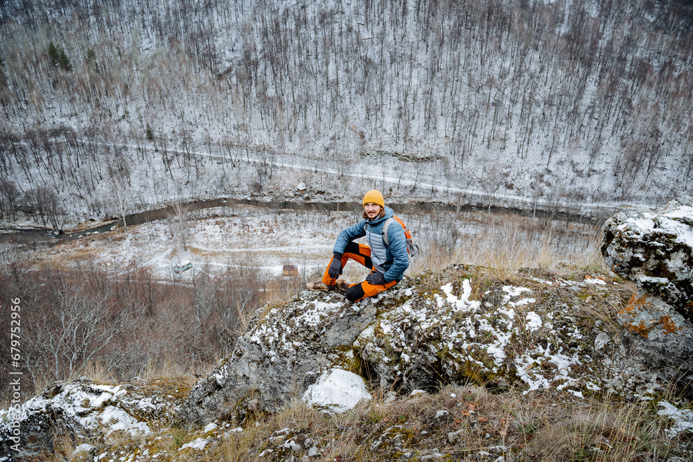 Obraz premium Top view of man sitting on cliff cliff, happy young man resting outdoors in autumn in mountains, gloomy weather, solo hike.