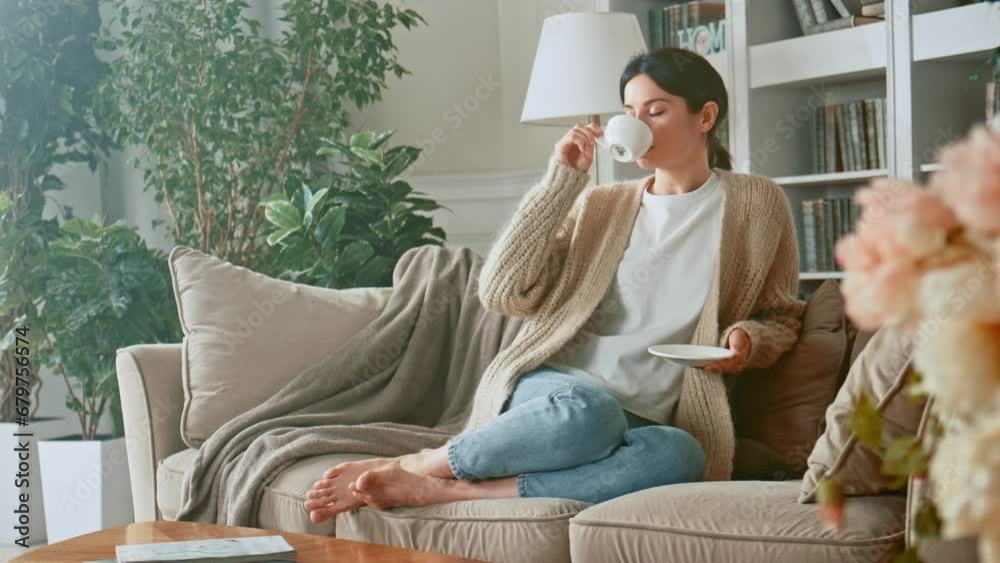 Relaxed woman drinking coffee or herbal tea and feeling carefree and refreshed while relaxing on the couch at home. Break time. Girl enjoying comfortable relaxing sitting on couch in the morning. 4K