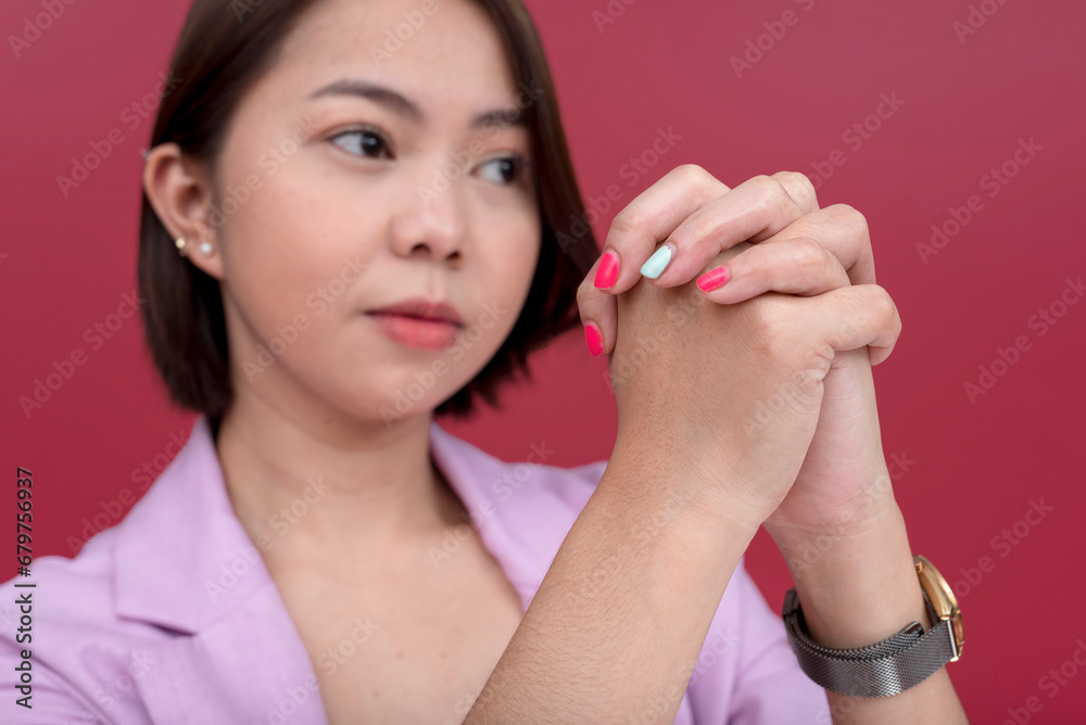 Candid shot of a young asian woman asking for help or a favor with hands clasped. Saying pretty please and pleading. Focus on hand. Studio shot with burgundy background. Candid shot of a young asian woman asking for help or a favor with hands clasped. Saying pretty please and pleading. Focus on hand. Studio shot with burgundy background.