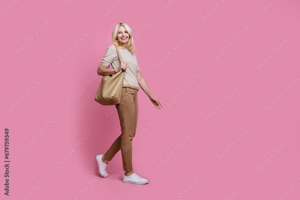 Full size profile portrait of gorgeous satisfied person hold bag walking empty space isolated on pink color background Full size profile portrait of gorgeous satisfied person hold bag walking empty space isolated on pink color background