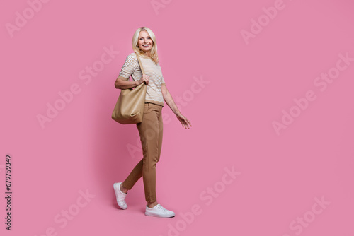 Full size profile portrait of gorgeous satisfied person hold bag walking empty space isolated on pink color background