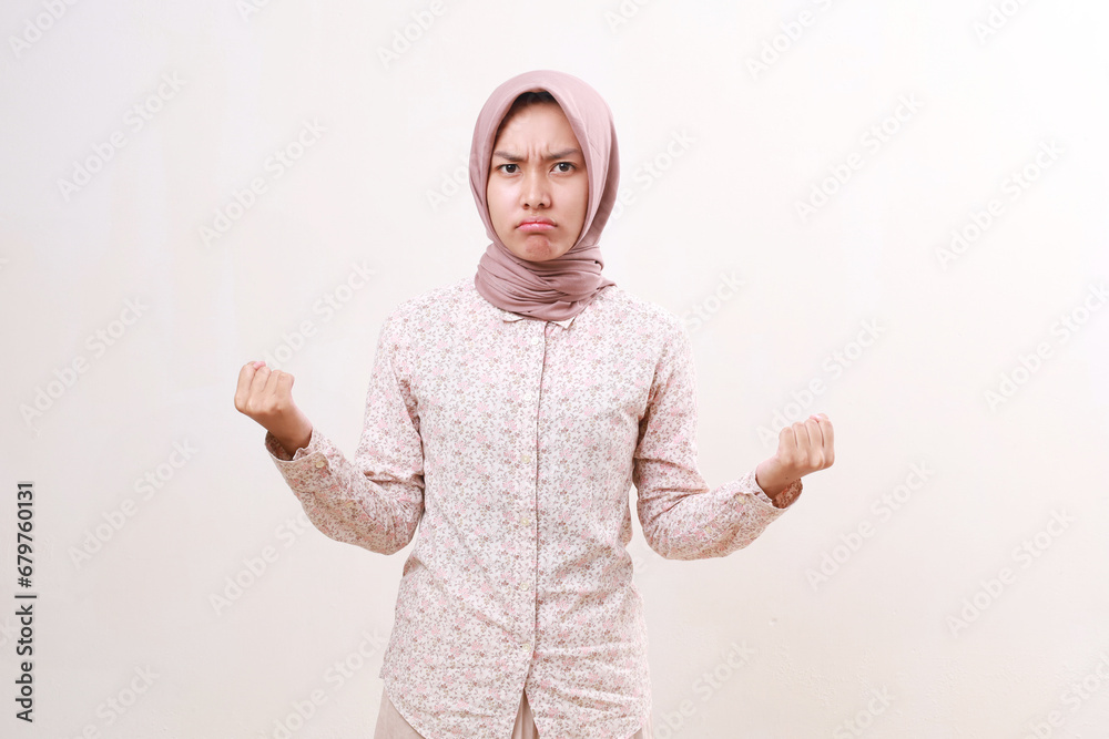 Angry unhappy young asian muslim woman looking at the camera with fist hands. Isolated on white Angry unhappy young asian muslim woman looking at the camera with fist hands. Isolated on white