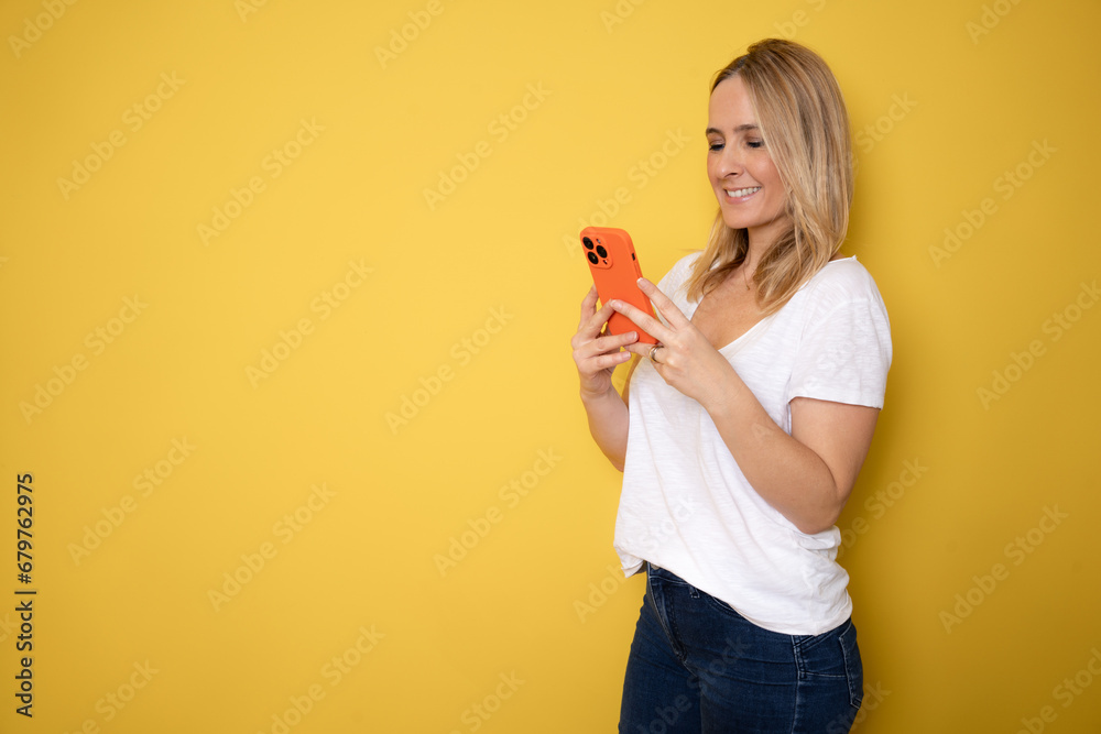 Young beautiful happy woman using smart phone. Excited surprised girl texting on her mobile phone. Studio shot isolated on yellow background. Technology, communication, social media concept Young beautiful happy woman using smart phone. Excited surprised girl texting on her mobile phone. Studio shot isolated on yellow background. Technology, communication, social media concept