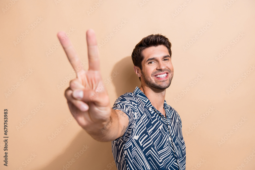 Photo of pleasant toothy beaming man with stylish haircut dressed print shirt showing you v-sign isolated on beige color background Photo of pleasant toothy beaming man with stylish haircut dressed print shirt showing you v-sign isolated on beige color background