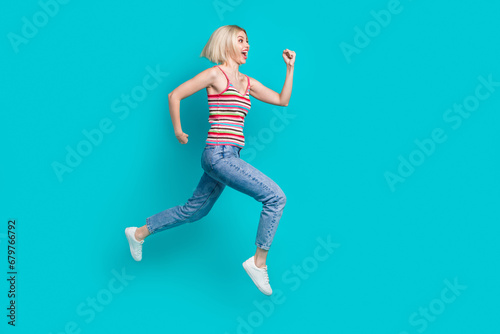 Full length photo of charming impressed girl dressed striped tank top running fast jumping high empty space isolated teal color background