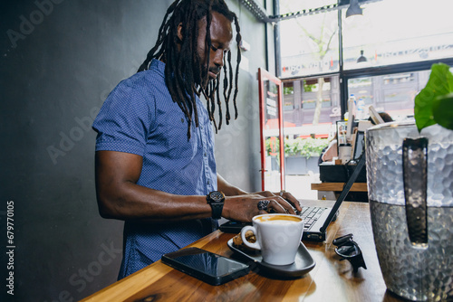 Freelance businessman with dreadlocks standing in coffee shop working on his laptop photo