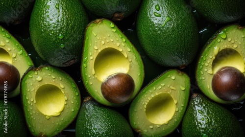  a pile of green avocados with drops of water on them and one cut in half to show the inside of the avocados.