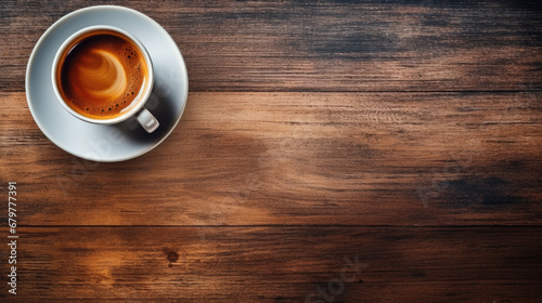 White coffee cup filled with coffee sits on a saucer surrounded by a large number of roasted coffee beans scattered on a dark wooden table, viewed from above in a flat lay composition.