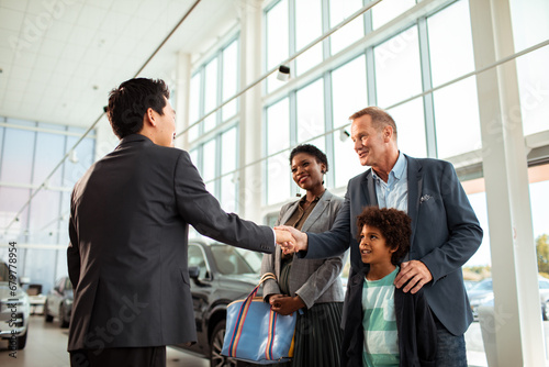 Salesman and Diverse Family Celebrating Purchase of New Car at Dealership photo