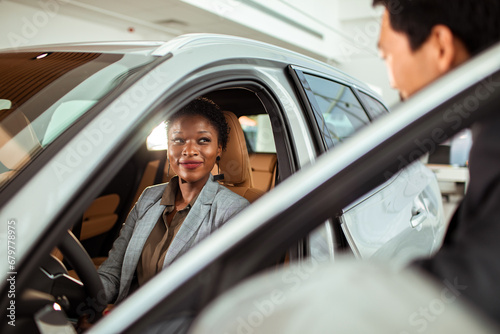 Young woman sitting in car looking at salesman in dealership photo