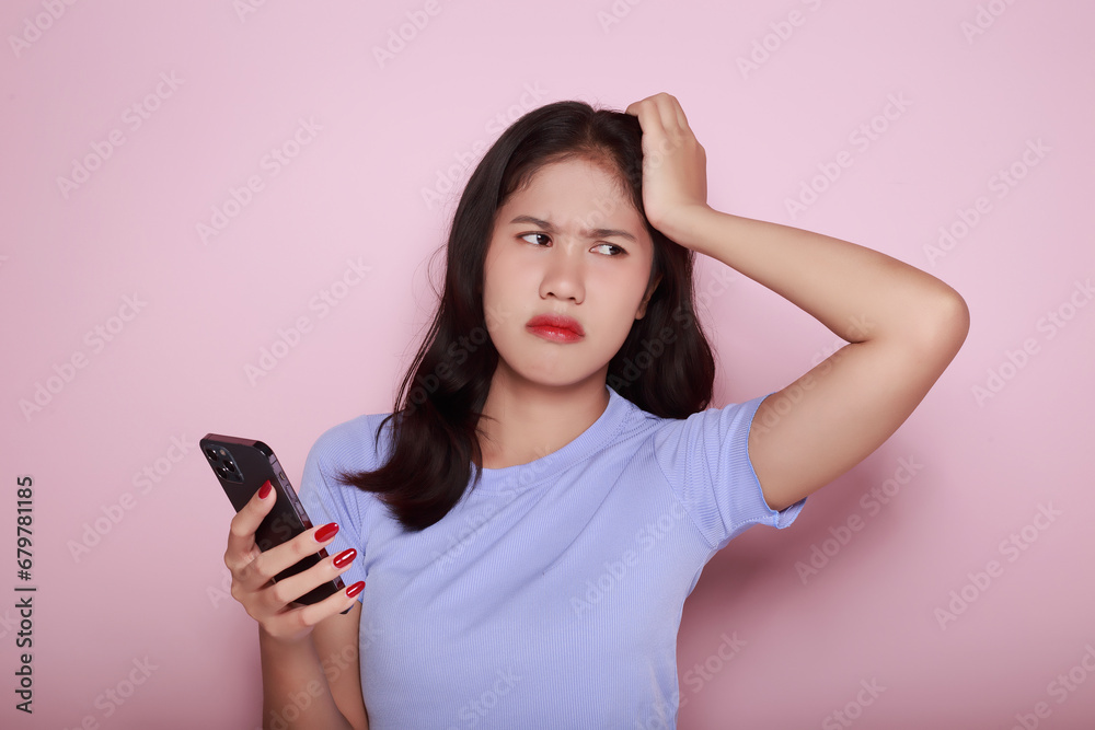 Young woman using the mobile with a serious expression, Portrait of a beautiful young woman in a light pink background, Asian woman posing using a mobile phone. Young woman using the mobile with a serious expression, Portrait of a beautiful young woman in a light pink background, Asian woman posing using a mobile phone.