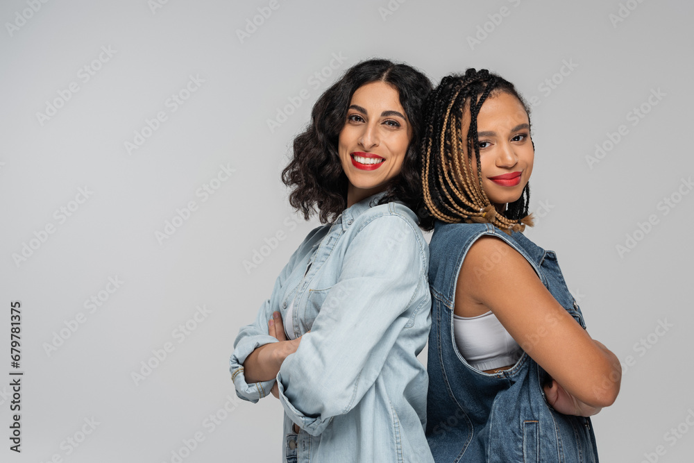 stylish multiracial women in denim outfits standing back to back with folded arms on grey, fashion stylish multiracial women in denim outfits standing back to back with folded arms on grey, fashion