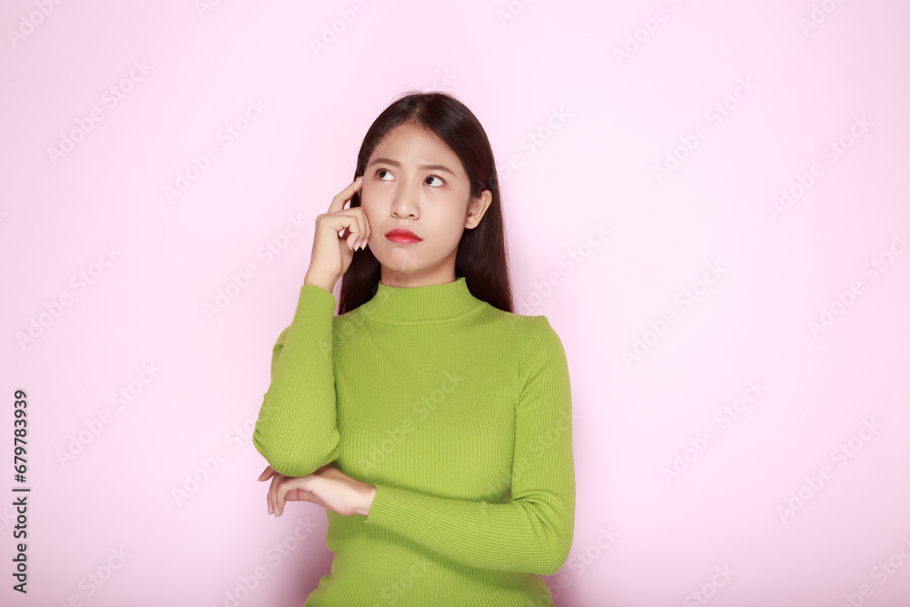 Asian woman making a thinking expression, Portrait of a young woman in a light pink background. Asian woman making a thinking expression, Portrait of a young woman in a light pink background.
