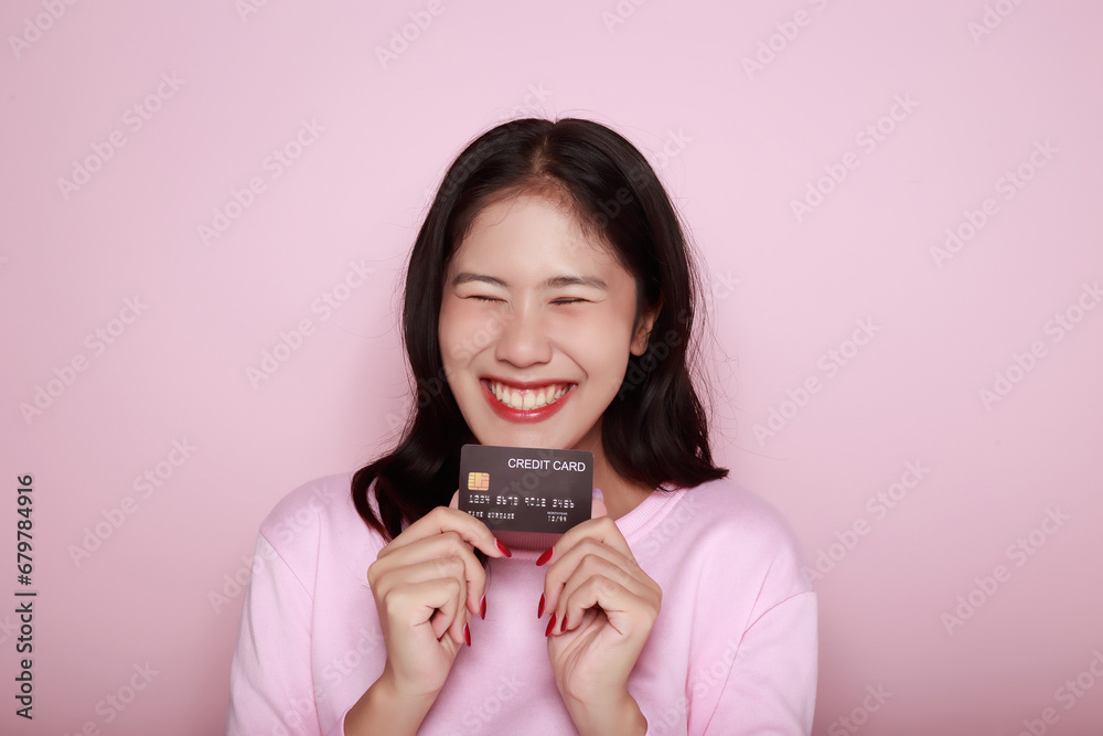 Asian woman holding a credit card in her hand Holding a debit card in hand A beautiful young woman was feeling very happy and excited. Portrait on a light pink background Asian woman holding a credit card in her hand Holding a debit card in hand A beautiful young woman was feeling very happy and excited. Portrait on a light pink background
