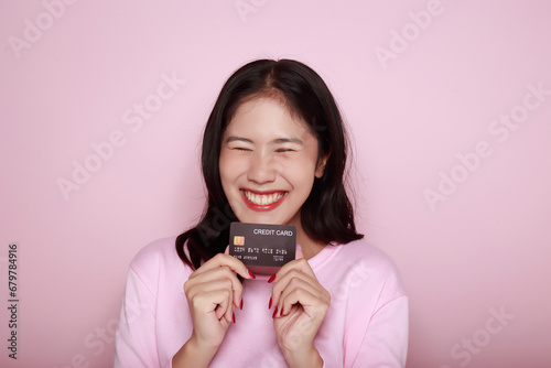 Asian woman holding a credit card in her hand Holding a debit card in hand A beautiful young woman was feeling very happy and excited. Portrait on a light pink background