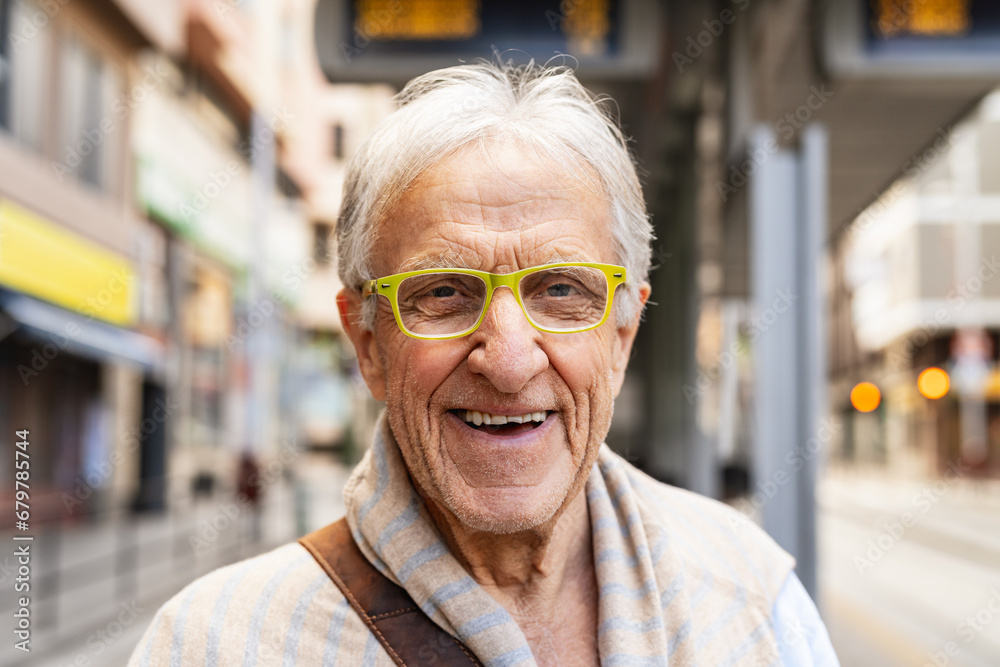 Happy senior man smiling in front of camera while waiting at tram station in the city Happy senior man smiling in front of camera while waiting at tram station in the city