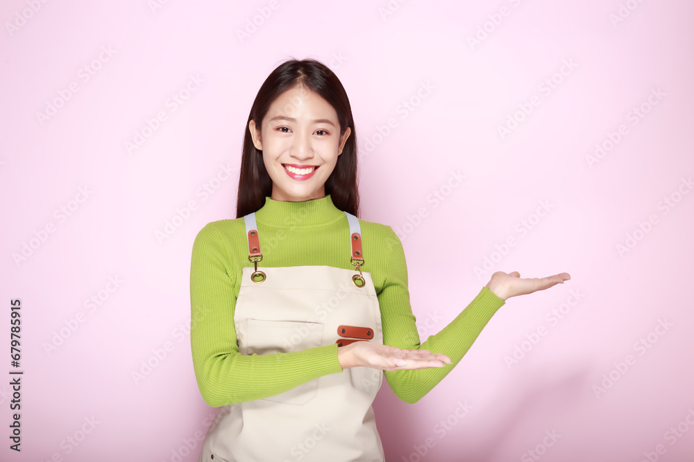 Standing and pointing happily, Portrait of a beautiful young woman in a light pink background, happy and smile, Young woman wearing an apron Standing and pointing happily, Portrait of a beautiful young woman in a light pink background, happy and smile, Young woman wearing an apron
