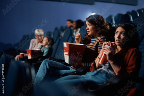 Young women watching horror movie in cinema.