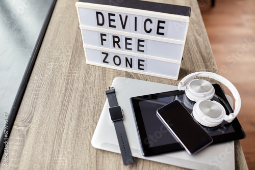 digital detox and technology concept - close up of device free zone words on light box and different gadgets on table at home