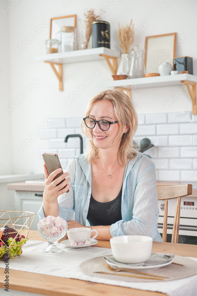 Smiling beautiful woman with cup of coffee and mobile phone in the kitchen