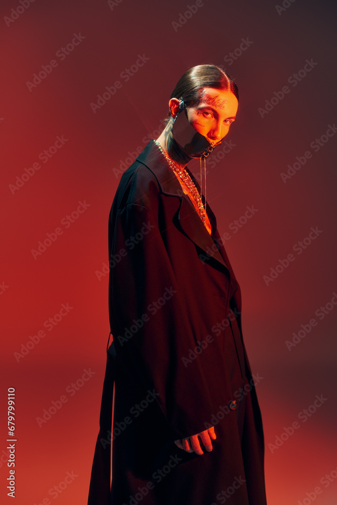 vertical shot of handsome sexy man in laced mask in black stylish attire surrounded by red light