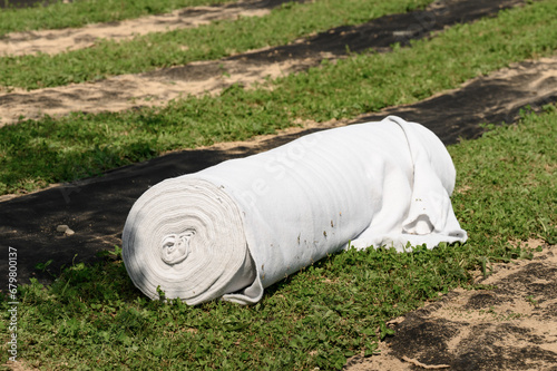 A roll of white geotextile lies on field. Preparation for drainage works. photo