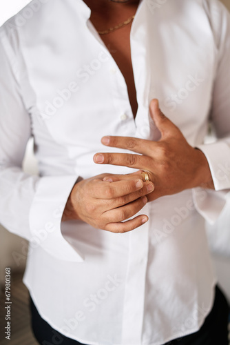 Groom in a white unbuttoned shirt adjusts the ring on his finger. Cropped. Faceless