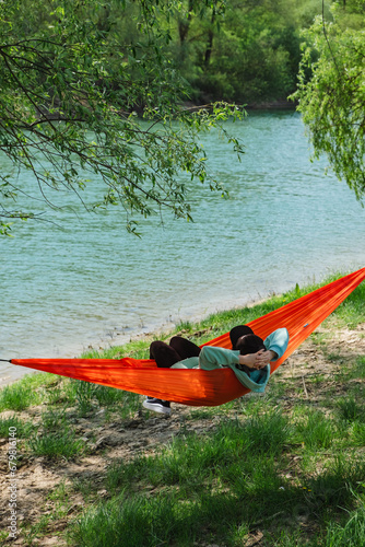 A woman in a cap lies in a hammock on the river bank