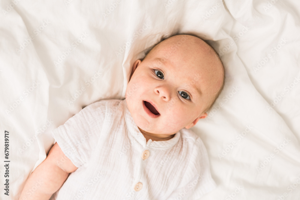 Adorable baby boy in white sunny bedroom. Newborn child relaxing in bed. Nursery for young children. Textile and bedding for kids. Family morning at home. Adorable baby boy in white sunny bedroom. Newborn child relaxing in bed. Nursery for young children. Textile and bedding for kids. Family morning at home.