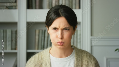 Portrait of young beautiful brunette girl at home in living room. Takes a deep breath, trying to calm his anger, and frustration. Woman with an angry face looking furious, mad and feeling frustrated photo
