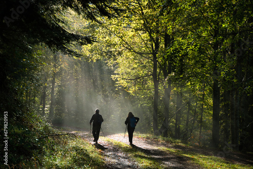 Spectacular beam of light in the forest early in the morning, showing two silhouettes of hikers. photo