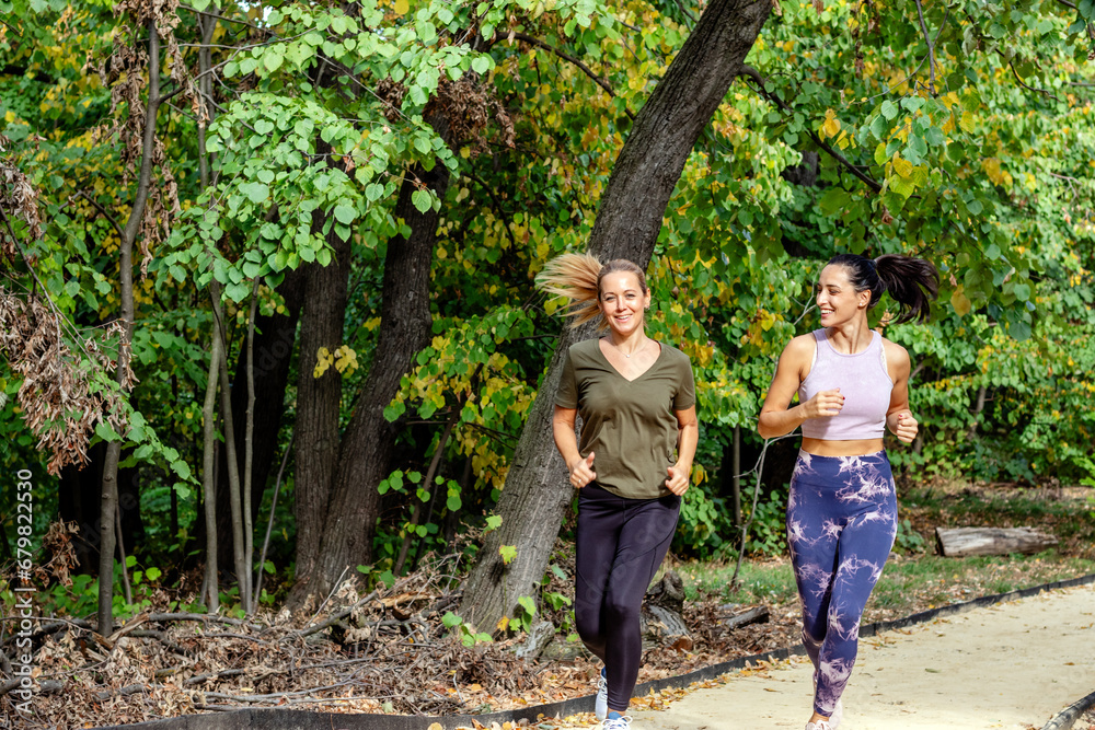 Obraz premium Two female joggers pursuing their activity outdoors. They are running on the jogging track in the park.