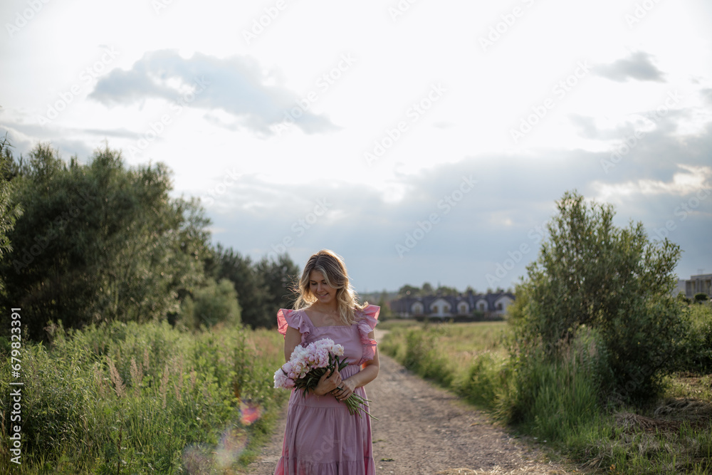 Romantic blonde in sundress with bouquet of soft pink peonies smiles,walks on summer day in nature. Romantic blonde in sundress with bouquet of soft pink peonies smiles,walks on summer day in nature.