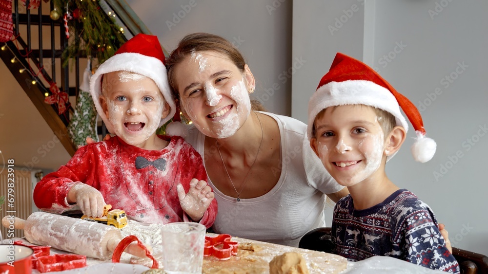 Portrait of happy funny family in Santa's hats got messy and dirty while preparing and cooking on kitchen for Christmas celebrations