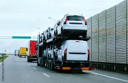 Car carrier trailer truck with brand new commercial vehicles for sale. New car delivery. Car transporter trailer loaded with many new cars for the customers. Two-level modular hydraulic semi-trailer