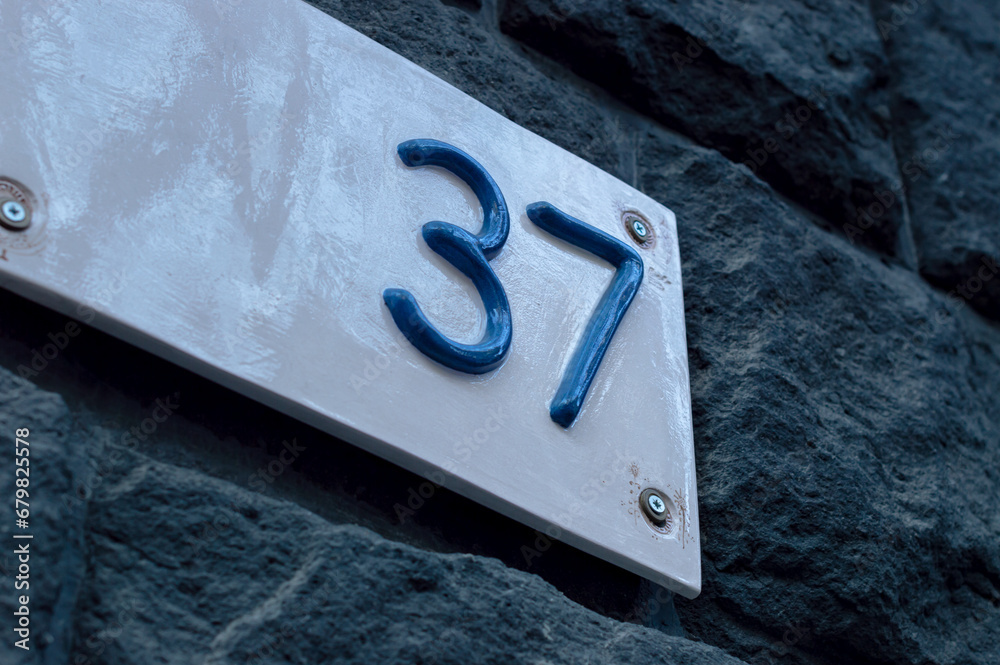 Number 37 building retro style white ceramic number plate with blue numbers, on the stone bricks background. Number 37 building retro style white ceramic number plate with blue numbers, on the stone bricks background.