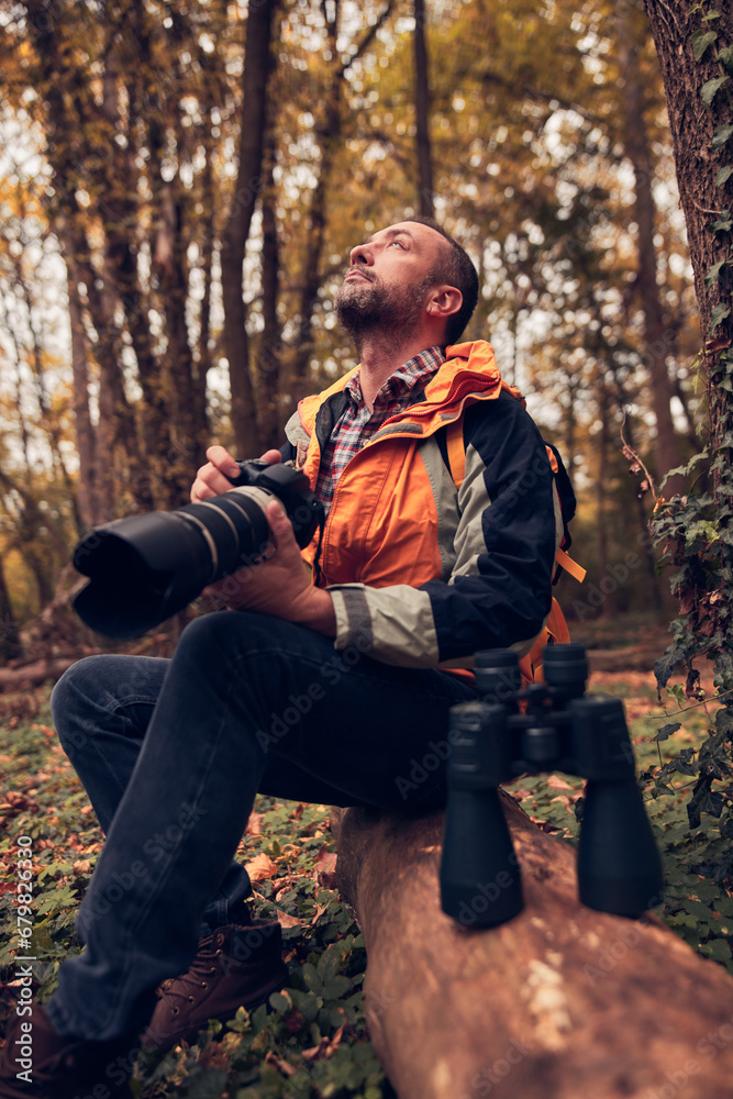 Man using binoculars and camera for bird and animal watching in nature.