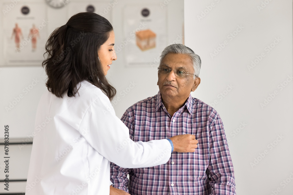 Senior Indian patient visiting medical practitioner woman for heart work checkup. Young Latin cardiologist doctor checking heartbeat rate of old man in clinic office, discussing health problems Senior Indian patient visiting medical practitioner woman for heart work checkup. Young Latin cardiologist doctor checking heartbeat rate of old man in clinic office, discussing health problems