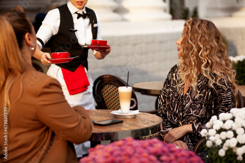 Two beautifully and elegant dressed girls are in the cafe and drink coffee in  the city. girlfriends laugh and spend time together. Womens frientship photo