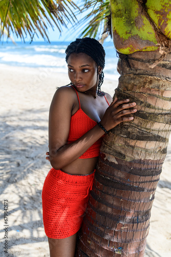 A portrait of a young african lady leaning against a coconut tree at a beach front