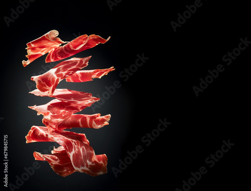 Thin slices of Spanish jamon flying in the air on black background. Traditional meat specialty of the local cuisine photo